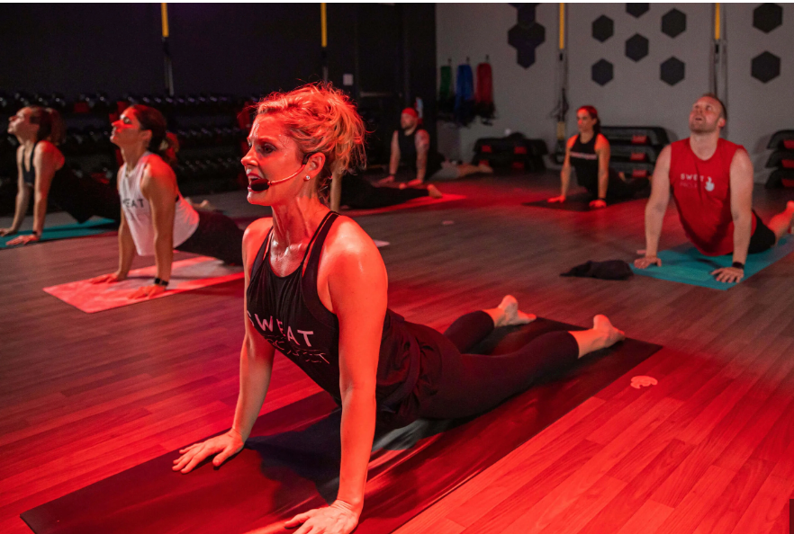 Woman leading a hot yoga workout class in a fitness studio warmed by the red glow of Striking Energy infrared heaters.