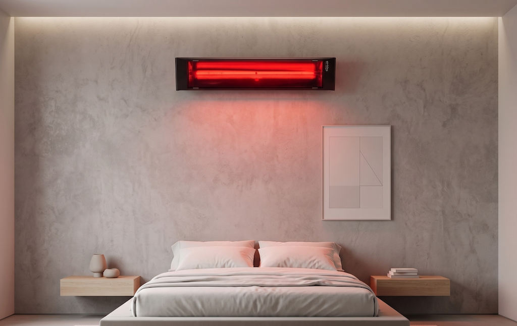 Modern black wall-mounted infrared heater glowing red above a bed in a bright white bedroom.