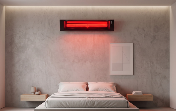 Modern black wall-mounted infrared heater glowing red above a bed in a bright white bedroom.