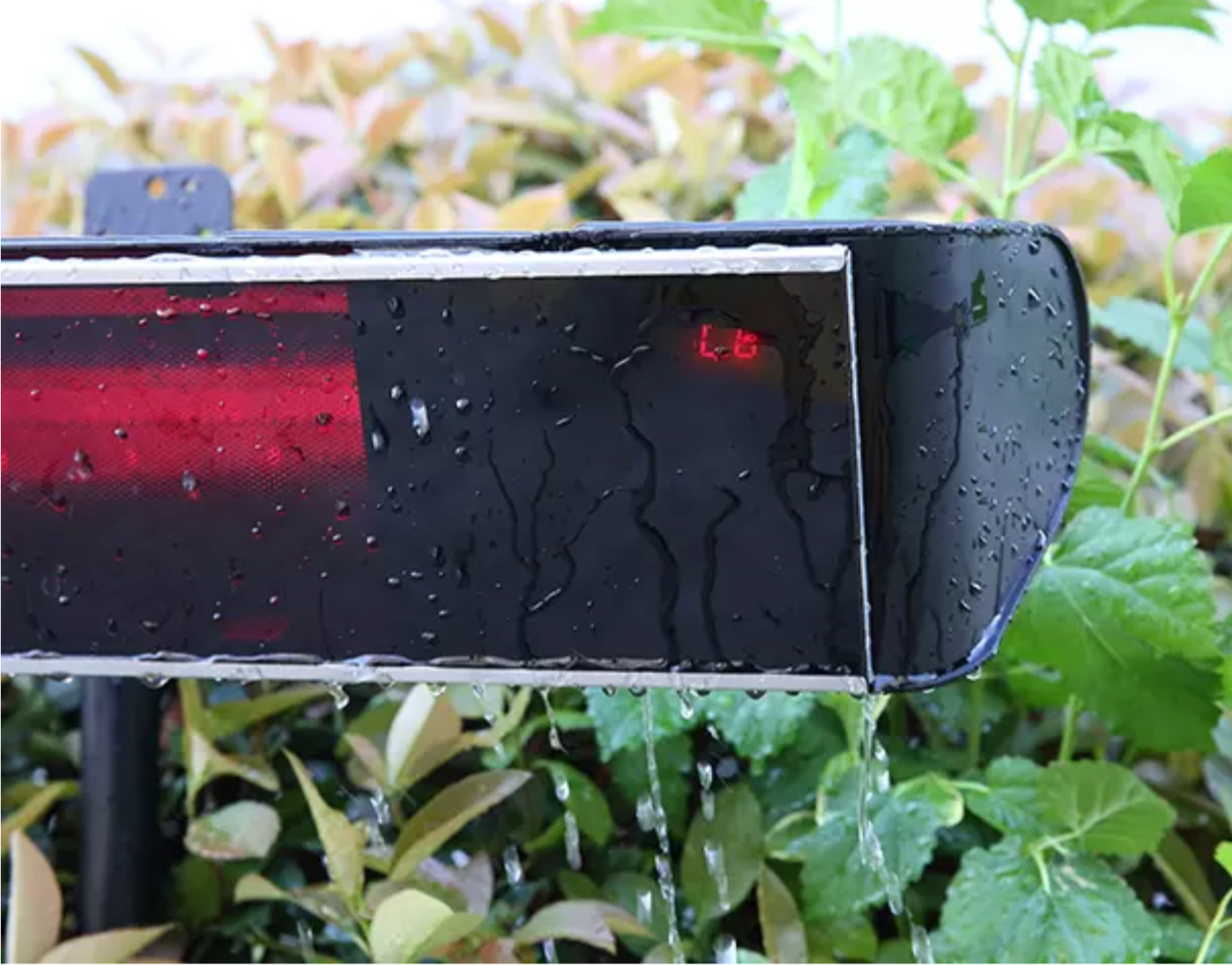 Close-up of a black weather-resistant outdoor patio infrared heater covered in water droplets